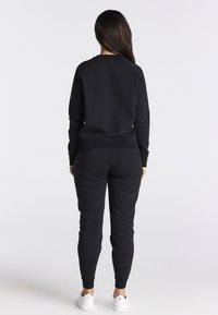 Felpa nera e pantaloni abbinati realizzati in tessuto morbido. Presentano una vestibilità rilassata, polsini a coste e orlo alla caviglia. Sneakers bianche completano l'outfit.