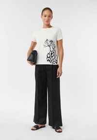 White cotton t-shirt with black tiger graphic and geometric patterns, paired with loose black trousers and a black drawstring bag.