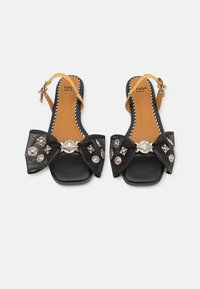 Mustat slingback-sandaalit, joissa on leveä kangashuiska, hopeiset yksityiskohdat ja neliönmuotoinen kärki. Ominaisuudet: vaalea sisäpohja ja keltainen nilkkaremmi.