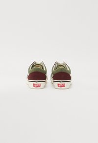 Två sneakers i bakvyn med en grön canvasöverdel och bordeauxfärgad mockahæl. Sulan är vit med en röd logodetalj.