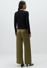 Zwarte geribbelde top met lange mouwen, gecombineerd met olijfgroene satijnen wijde broek en zwarte haksandalen, met een gladde textuur en elegante uitstraling.