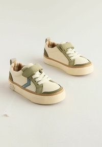 Børnesneakers med hvid bund, grønne accenter, struktureret gummisål, snørebånd og velcro-rem; ternet foring og logo detaljer.