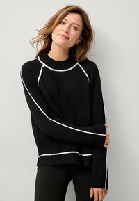 Maglione nero a maglia con collo alto, strisce bianche di accento lungo le spalle e le braccia, e polsini e orlo a costine.