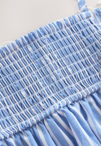 Blåt og hvidt stribet stof med smockdetaljer øverst. Teksturen er samlet, hvilket giver strækbarhed og et flydende udseende.