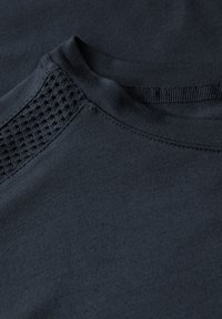 T-shirt bleu marine foncé avec une texture lisse, un col rond et un accent en maille à motif sur l'épaule pour la respirabilité.