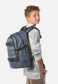 Modrý batoh s polstrovaným zádovým panelem a nastavitelnými popruhy, obsahující boční kapsy, vrchní madlo a texturovaný vzor na přední straně.