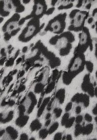 Sciarpa con stampa leopardata caratterizzata da una texture morbida, prevalentemente grigia con motivi neri e estremità frangiato.