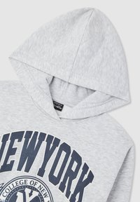 Felpa grigia con una texture morbida, caratterizzata da una grande stampa "NEW YORK" in blu navy. Include un cappuccio e dettagli a coste vicino al colletto.