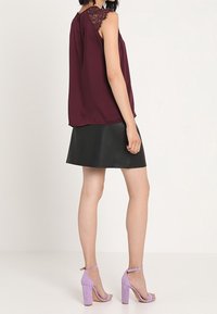 Top sin mangas burdeos con adornos de encaje, combinado con una minifalda de cuero negra y sandalias de tacón alto en color lavanda. Tejido suave y silueta estructurada.