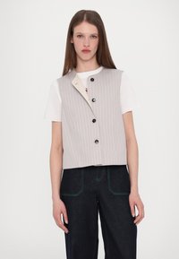 Gilet coupé en tissu gris clair avec des rayures verticales, comportant un devant à bouton, un col contrastant et des poches latérales. Porté par-dessus un t-shirt blanc.