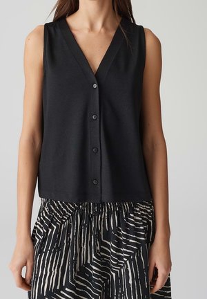 Czarny top bez rękawów zapinany na guziki z dekoltem w serek, zestawiony z czarno-białą, abstrakcyjnie paskowaną spódnicą z elastycznym paskiem w talii.