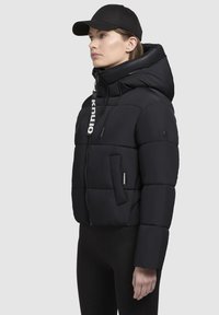 Svart puffjacka med en kortad design, horisontellt kviltad textur, justerbar huva och ficka med dragkedja framtill; har en framträdande logotypdetalj.