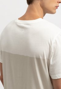 Lichtgrijs T-shirt met korte mouwen en een zachte, gladde textuur. Heeft een subtiele donkergrijze horizontale lijn en een klein logo op de achterkant.