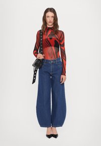 Top lung cu mâneci lungi, ajustat, roșu și negru, cu un model ondulat, asortat cu blugi largi albaștri și pantofi cu vârf ascuțit negri. Geantă de umăr neagră cu cuie.