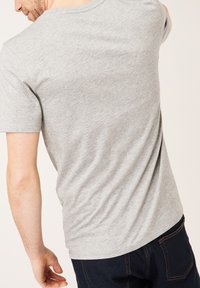 Graues Kurzarm-T-Shirt, von hinten präsentiert, mit lockerer Passform und glatter Textur, kombiniert mit dunklen Jeans, die Taschen zeigen.
