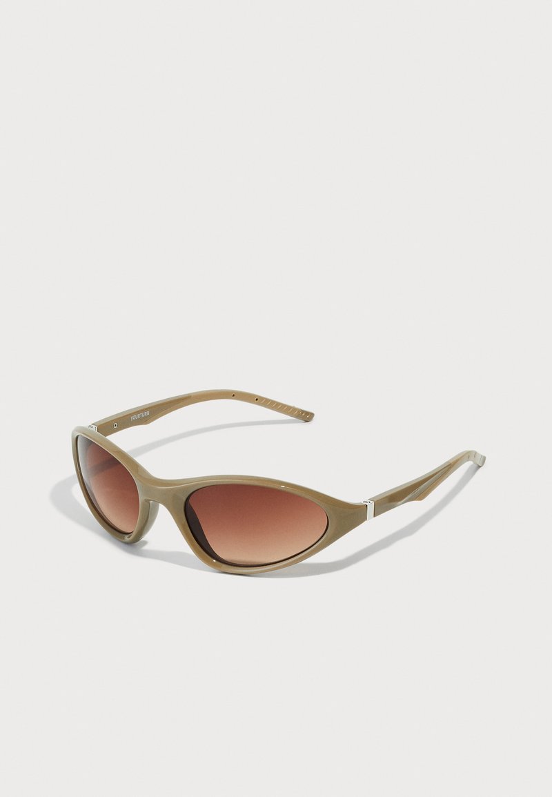 Καφέ γυαλιά ηλίου με γραδάρισμα, με γυαλιστερό πλαστικό σκελετό σε ελιά πράσινο χρώμα, σε επι elongated σχήμα, και λεπτούς βραχίονες με διακριτικές λευκές λεπτομέρειες.