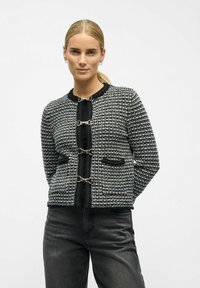 Schwarze und weiße Tweed-Cardigan mit rundem Ausschnitt, Fronttaschen und goldfarbener Hardware-Verschluss. Strukturierter Stoff mit kontrastierendem schwarzen Saum.