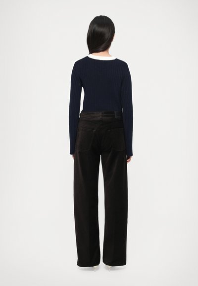 Bluza bleumarin cu mâneci lungi, cu dungi, asortată cu pantaloni negri din catifea cu talie înaltă și croială largă. Ținuta are un design curat și simplu.