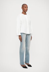 Blusa branca de manga longa, de corte solto, com decote redondo; combinada com jeans de perna reta em azul claro e sapatos de salto preto com bico fino.