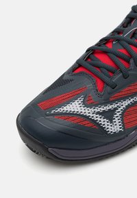 Buty sportowe z przewagą granatowej i czerwonej siateczki, o teksturowej powierzchni i białych odblaskowych akcentach. Sznurowana konstrukcja z wzmocnionym noskiem.