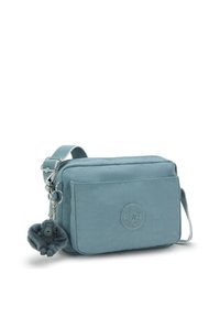 Borsa a tracolla azzurra chiaro realizzata in tessuto resistentewater, con chiusura a zip, una tasca frontale e un portachiavi a forma di scimmietta pelosa.