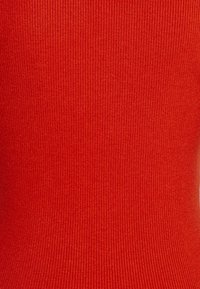 Czerwona dzianina prążkowana o gładkiej, fakturowanej powierzchni. Charakteryzuje się pionowym wzorem pasków i dopasowanym fasonem.