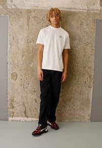 Bílá krátký rukáv Puma tričko, černé džíny a černé tenisky s červenými akcenty. Hladká tkanina a přiléhavý střih. Jednoduchý design.