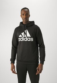 Czarna bluza z kapturem wykonana z miękkiego materiału, z dużym białym logo Adidas. Posiada kaptur ze sznurkiem oraz ściągacze na mankietach i u dołu.