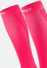 Kompressionssocken in einem leuchtenden Pink, mit einer gerippten Struktur und einer glatten Oberfläche. Weiße Markenzeichen oben sorgen für einen Kontrast.