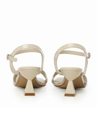Beige glanzend leren sandalen met een open achterzijde, kleine driehoekige hakken en dunne enkelriemen met gespsluiting.