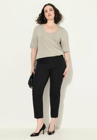 Lichtgrijze scoop-neck top met korte mouwen, gecombineerd met een aansluitende zwarte broek en zwarte hakken met gouden accenten. Zwarte tas in de hand.