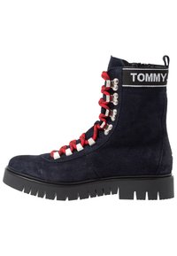 Námořnické semišové kotníkové boty s červenými tkaničkami, stříbrnými očky a černou gumovou podrážkou. Vyznačují se logem na vrchu a odolným dezénem.