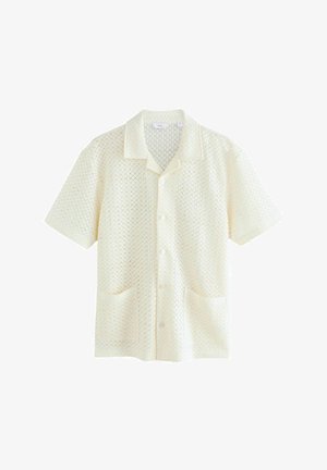 Kremin krāsas īsām piedurknēm krekls ar teksturētu dimanta rakstu, aprīkots ar izgrieztu apkakli, piecām pogām un divām priekšējām kabatām.