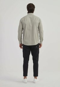 Chemise rayée en vert clair et crème, manches longues, col boutonné. Assortie à un pantalon noir fuselé et des chaussures blanches.