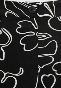 Pantalons en tissu noir avec un motif de lignes abstraites blanches, une fermeture à bouton à l'avant et une texture lisse avec des détails de couture visibles.