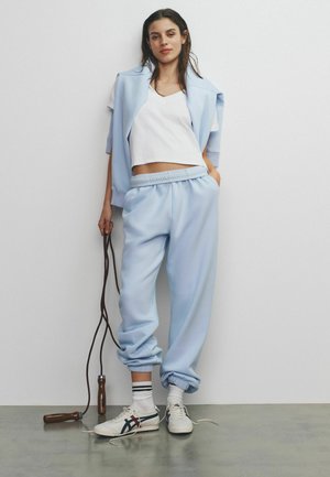 Vaaleansininen huppari ja siihen sopivat verkkarit, yhdistettynä valkoiseen lyhyeen toppiin. Varustettu joustavalla vyötäröllä, resorilla varustetuilla hihoilla ja kuntohyppynarulla.