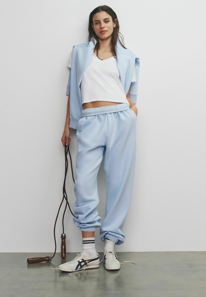 Svetlomodrá mikina a rovnaké tepláky v kombinácii s bielym crop topom. Má elastický pás, rebrované manžety a fitness švihadlo.