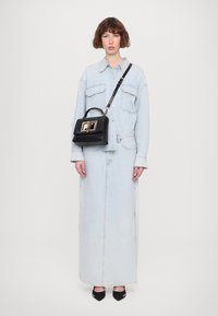 Lys blå denimjakke og skjørt med en svart håndveske som har gull detaljer, brukt med svarte spisse hæler.