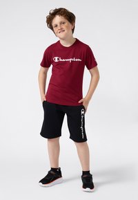 Röd bomull t-shirt med vit "Champion" logga, kombinerad med svarta shorts med vit "Champion" märkning. Svarta sportskor med accenter.