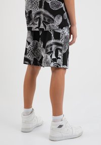 Pantalones cortos negros con un atrevido patrón abstracto blanco, combinados con zapatillas altas blancas. Los pantalones cortos son de longitud hasta la rodilla y tienen un corte relajado.