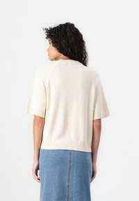 Crème sweater met korte mouwen en een geribbelde zoom en halslijn, met een zachte textuur, gedragen over een lichtblauwe denim rok.