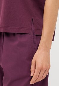 Bordeaux katoenen top met zijsplitten aan de onderkant, gecombineerd met bijpassende paarse broek, die een soepele textuur en een relaxte pasvorm laten zien.