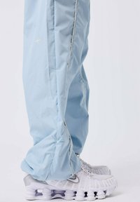 Lichtblauwe joggingsbroek van soepel materiaal, met subtiele witte bies en een sterdetail. Gecombineerd met witte sportschoenen met een onderscheidende zool.