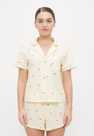 Lichtgele korte pyjamapakket met een V-hals en een klein borstzakje. Heeft een subtiel streeppatroon en verspreide bladmotiieven in het oranje.