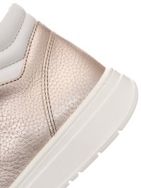 Nahaufnahme der Ferse eines metallischen roségoldenen Sneakers mit strukturiertem Leder und weißen, gepolsterten Sohlen-Details vor einfarbigem Hintergrund.