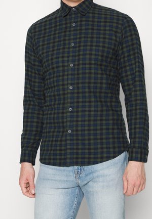 Dlouhá košile s kostkovaným vzorem v tmavě zelené a námořnické modři, zapínání na knoflíky, s klasickým límečkem a slim fit střihem. Textura bavlněné látky.