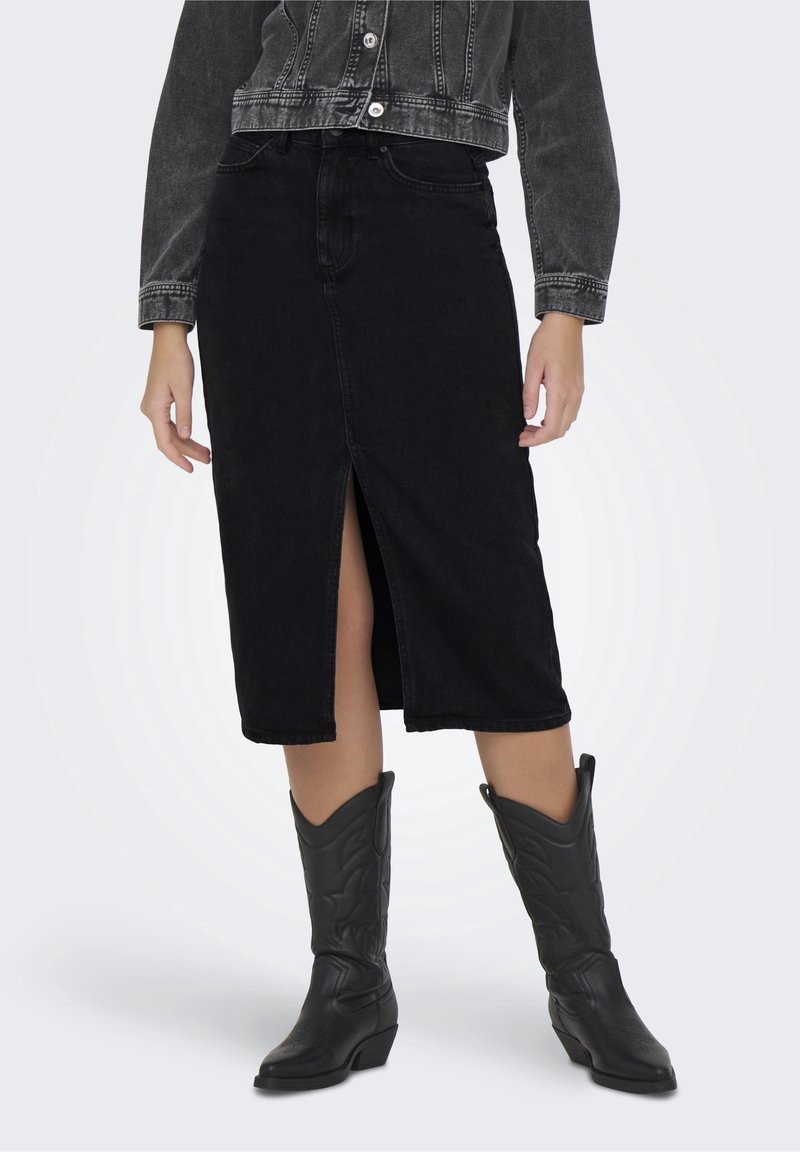 Jupe en denim noir avec une fente à l'avant, associée à des bottes de cowboy noires. La jupe présente une taille cintrée et une silhouette droite.