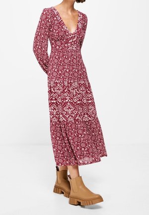 Czerwona długa sukienka w wzory z dekoltem w serek i długimi rękawami, zdobiona motywami kwiatowymi, zestawiona z beżowymi botkami na grubej podeszwie.