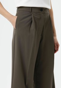 Wide-legged trousers in dark olive green fabric, featuring front pleats, a single button closure, and side pockets. Smooth texture.