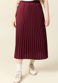 Burgundy plisserad midiklänning med resårmidja, slät textur och flödande design. Buren med vita sneakers och ribbade strumpor.